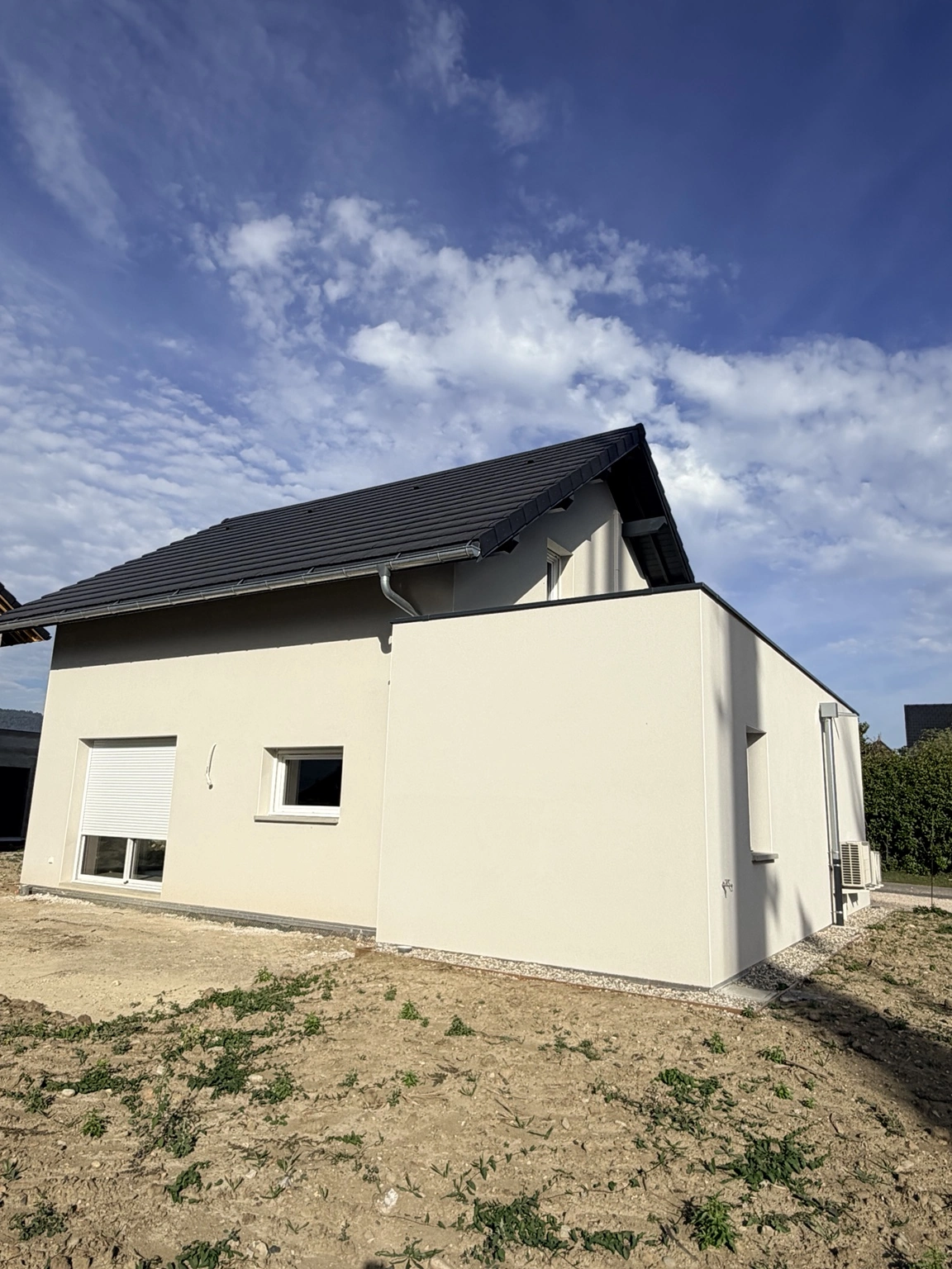 Façade latérale : enduit clair et lignes de toiture foncées.